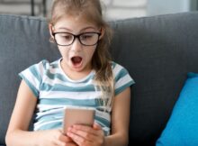 Child girl looking at mobile phone at home, with a surprise expression on her face