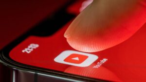 Finger touches the Youtube application on smartphone screen on red background