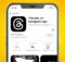 An iPhone on an orange background showing the App Store download page for the Threads app