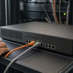 An unbranded firewall appliance on a maintenance shelf, with Ethernet cables leading toward server equipment.